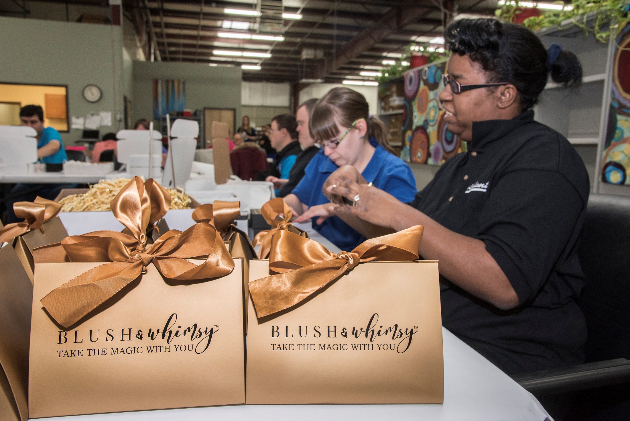 Adelante Development Center team members preparing Blush & Whimsy ribboned gift bags